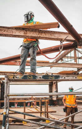 man in blue denim jeans and blue denim jacket standing on orange metal bar during daytime